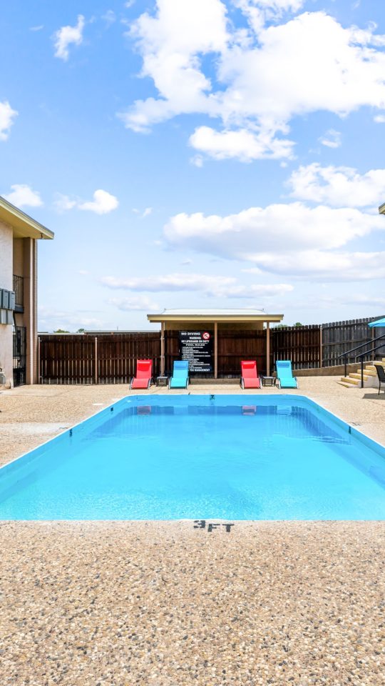 a pool with lounge chairs and a patio area at The Alamo Village Apartments