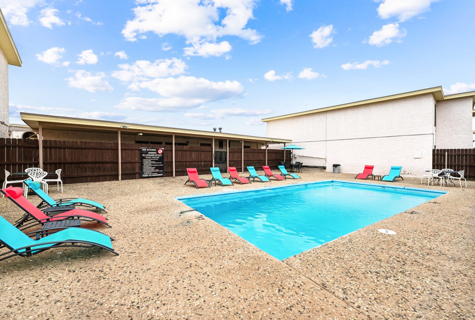 a pool and lounge chairs in front of a house at The Alamo Village Apartments